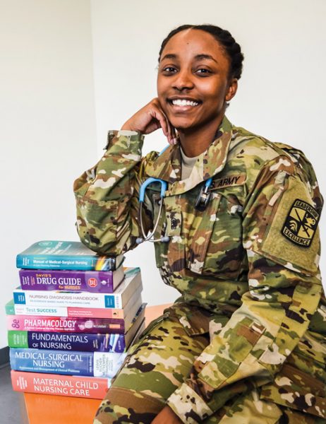 Destinee Wesley in army uniform with a stethoscope around her neck sitting next to a stack of medical textbooks